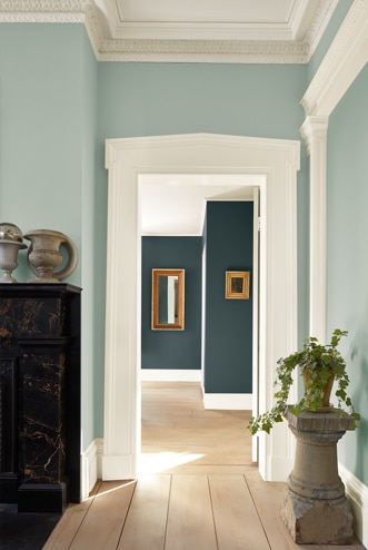 Ce couloir vert pâle au plancher de bois mène à une pièce aux murs sarcelle éclatant et miroirs décoratifs.