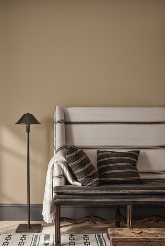 Banc rembourré de tissu blanc aux rayures noires avec coussins assortis contre un mur marron clair avec lampe sur pied noire.