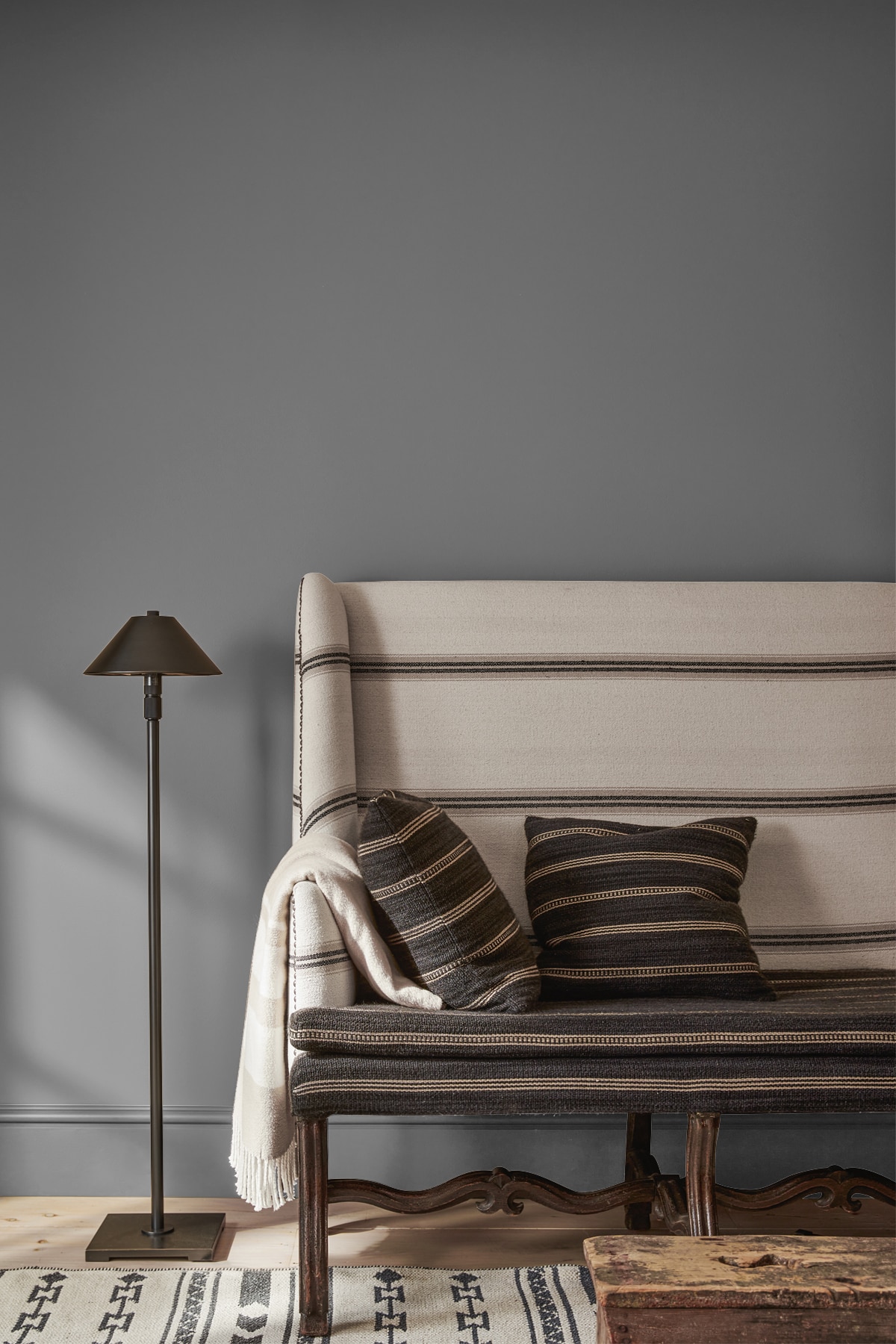 Banc rembourré de tissu blanc aux rayures noires avec coussins assortis contre un mur marron clair avec lampe sur pied noire.